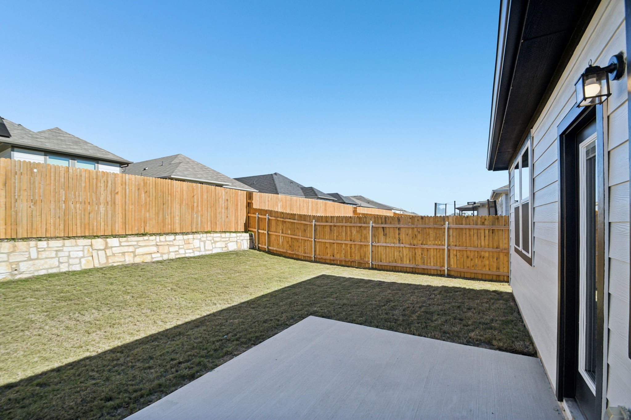 A fenced in yard with a house and a stone wall.