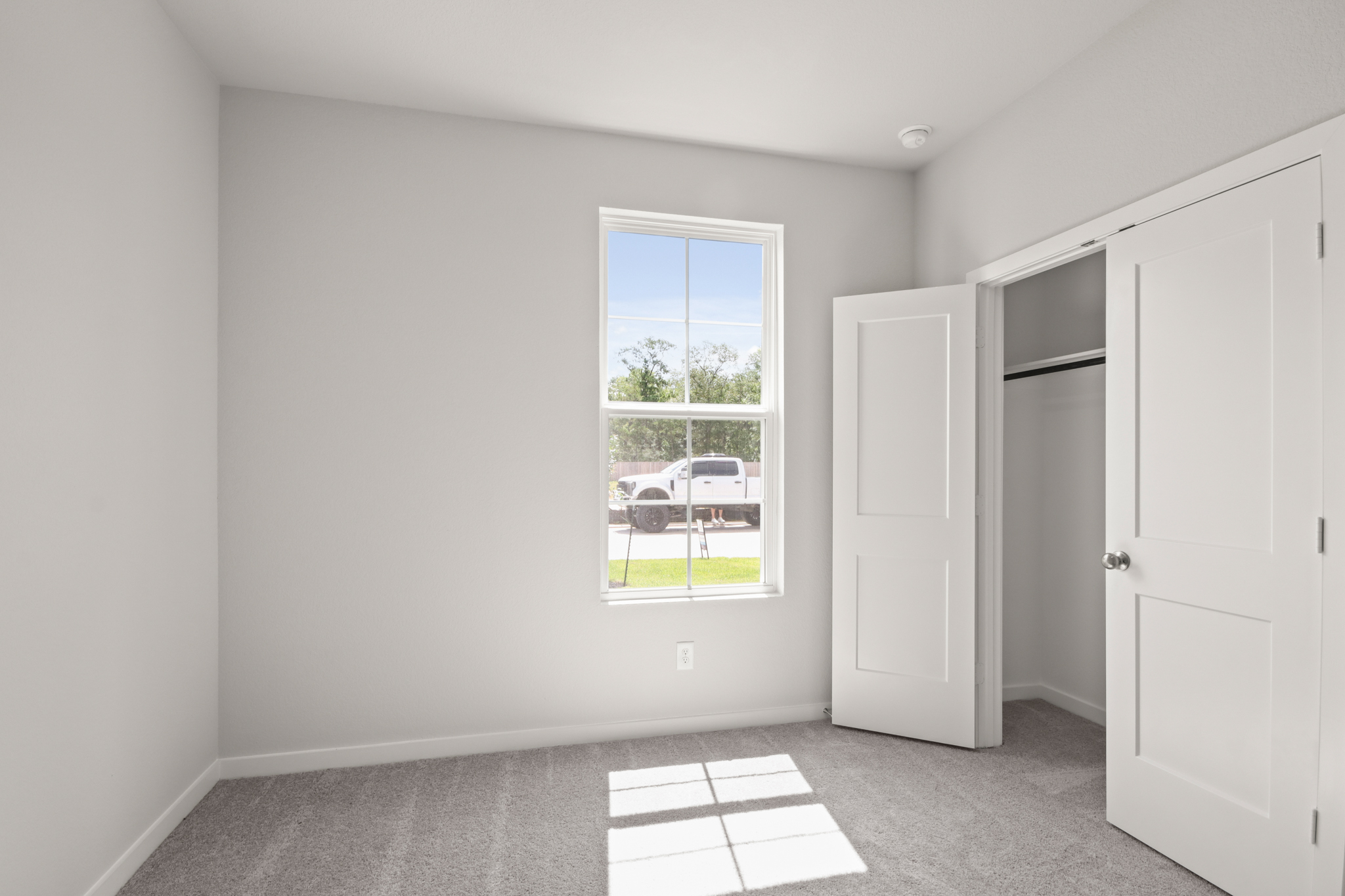 A room with white walls and a window with a car outside.