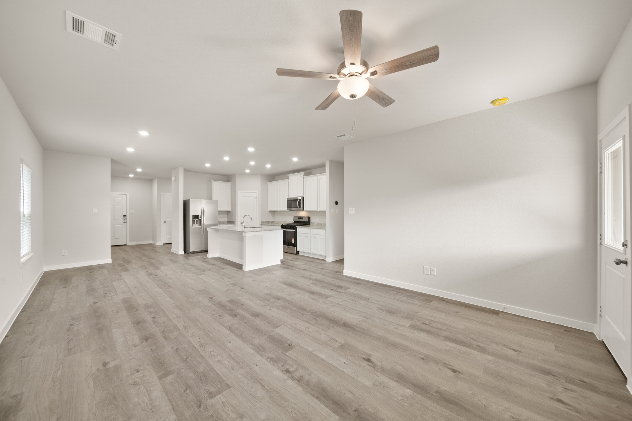 A large empty room with a ceiling fan and a wood floor.