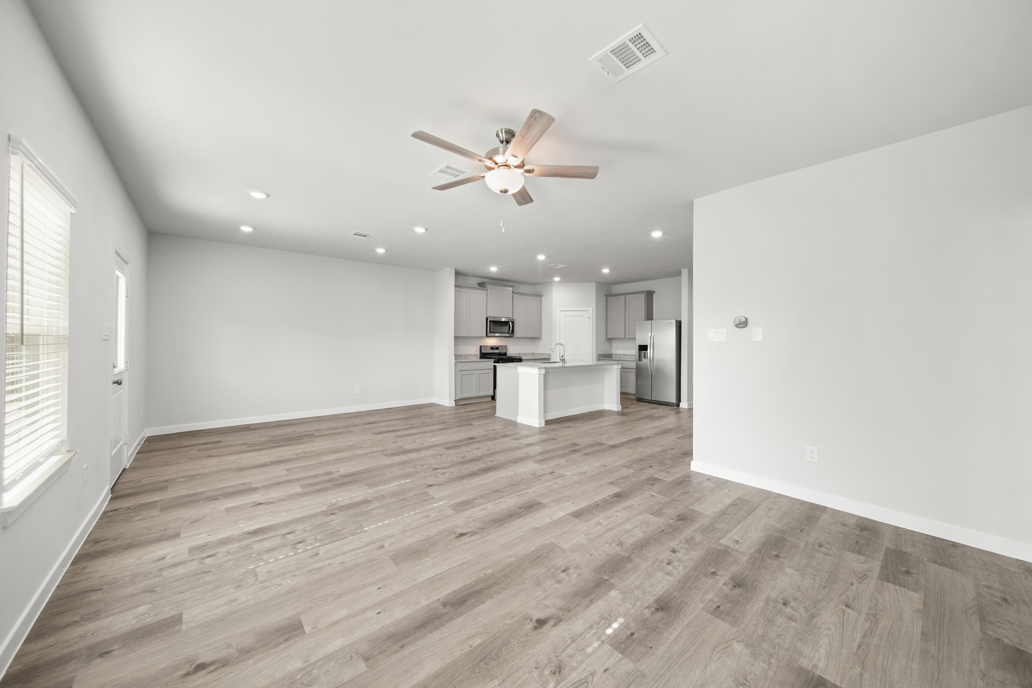 A large empty room with a wood floor and a ceiling fan.