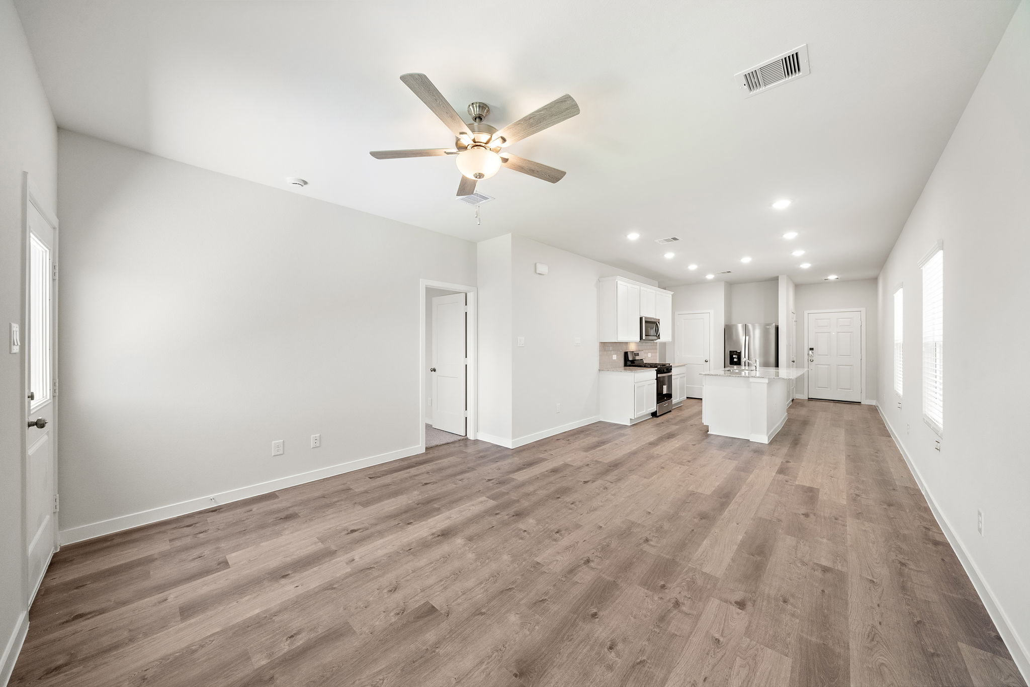 A large empty room with a ceiling fan and wood floors.