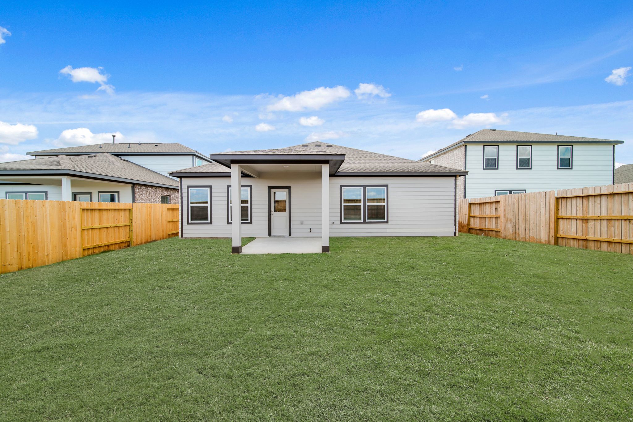 A green lawn with a fence and a house in the background.