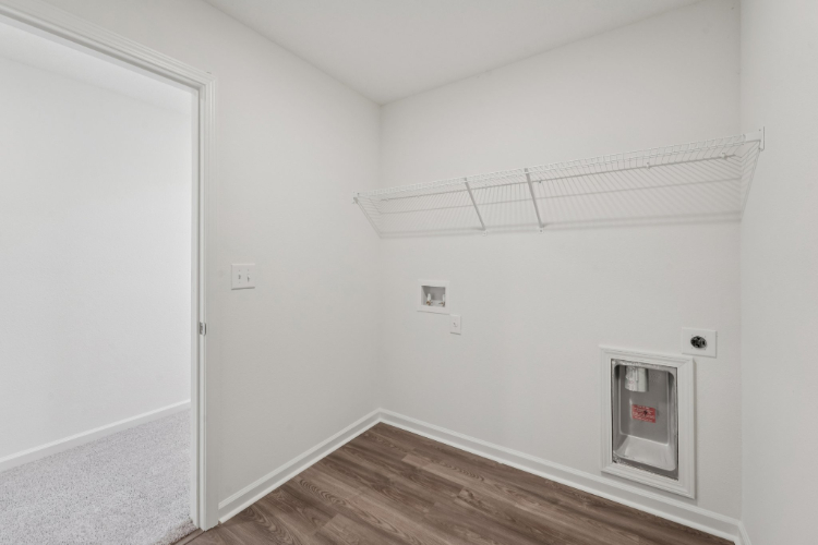 A room with a wood floor and a white wall with a vent.